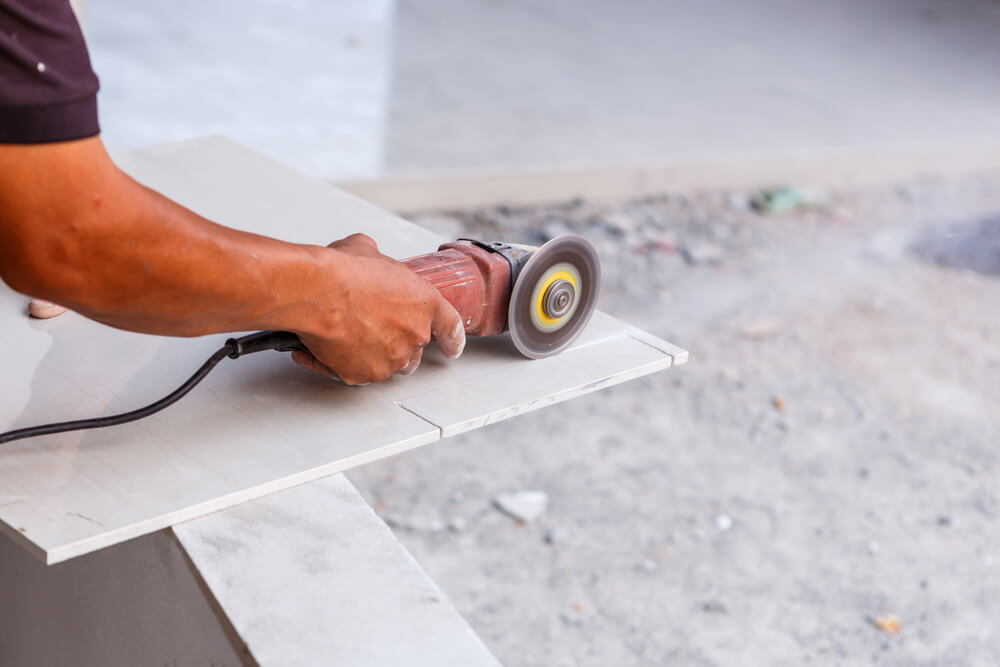 a tiler cutting the end off a white tile with a tile cutting grinder